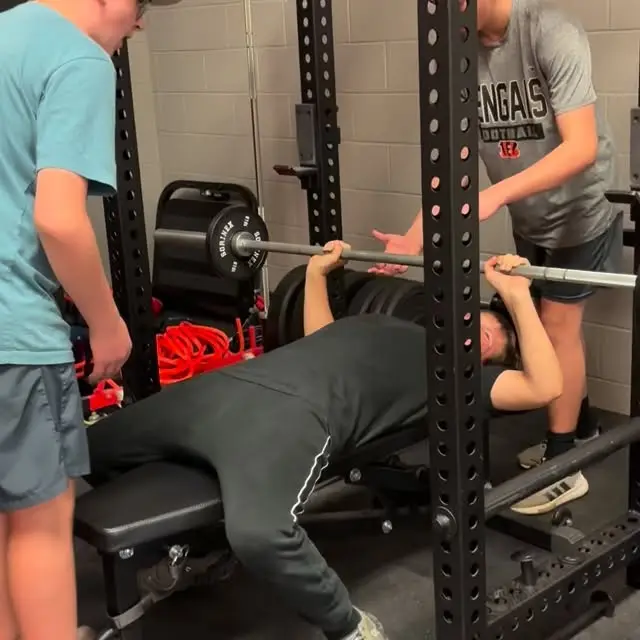 Teen bench pressing with two teen spotters