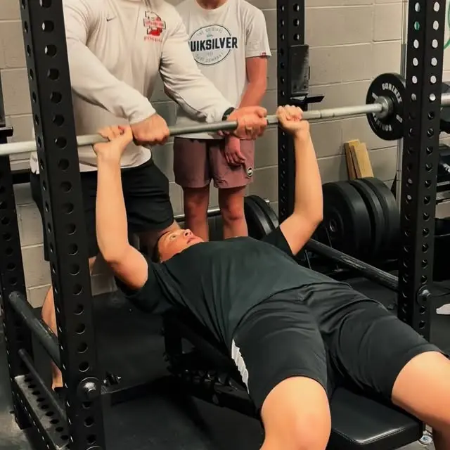 Teen bench pressing with a coach spotting the bar