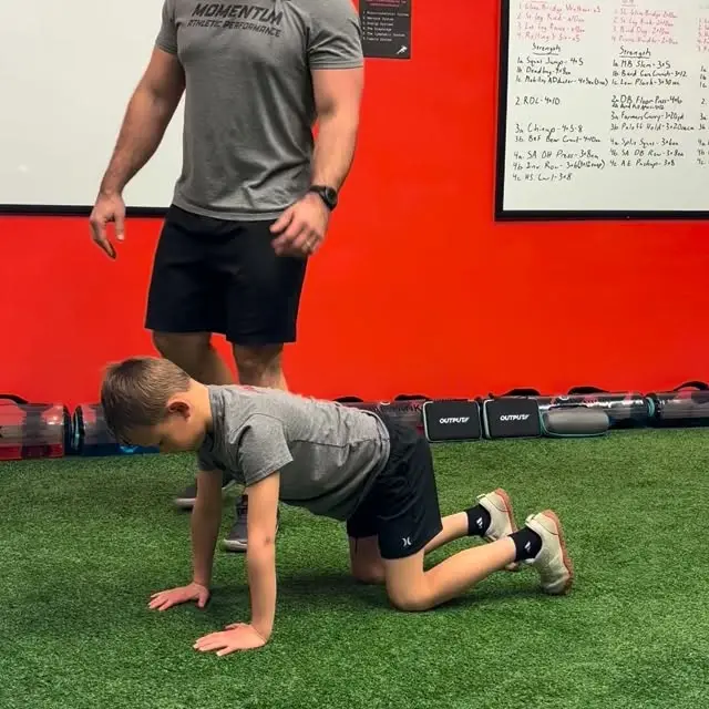 Young athlete doing a quadruped hip drill with a coach