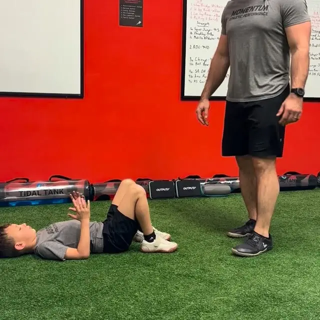 Young athlete doing a glute bridge with a coach