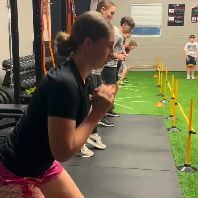 A line of Momentum athletes attacking an agility-pole drill across the turf together
