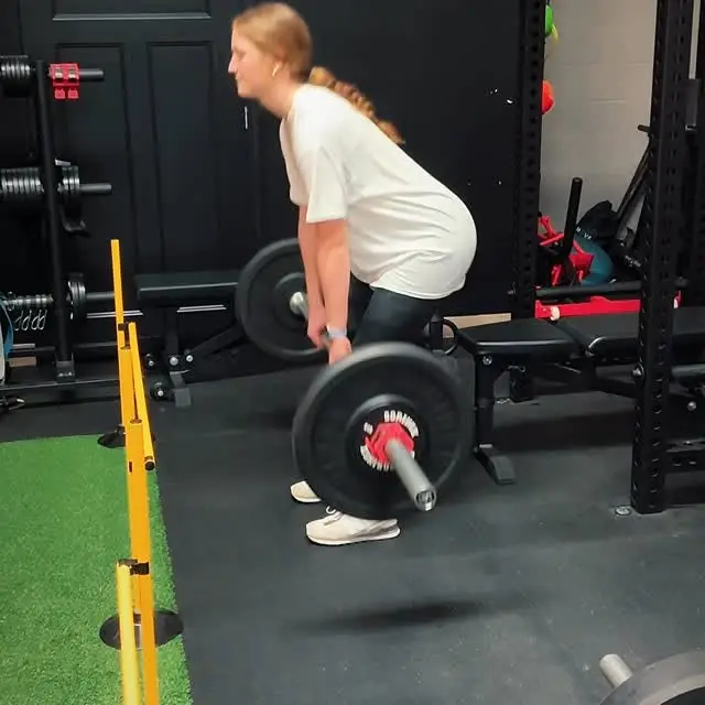 Teen athlete deadlifting a barbell on the black floor