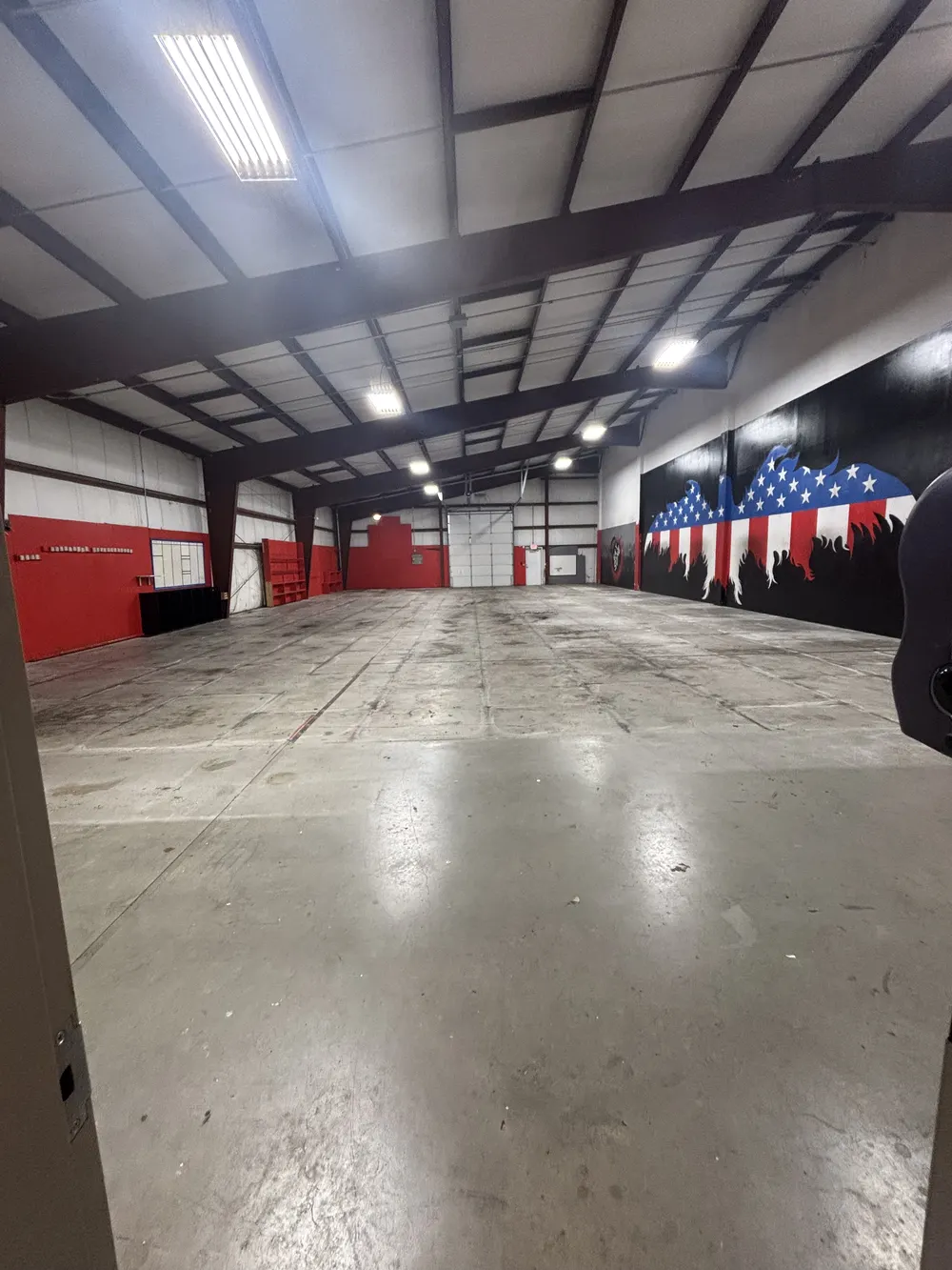 Looking down the full length of the empty building toward the loading door, red walls on the left and the eagle mural on the right