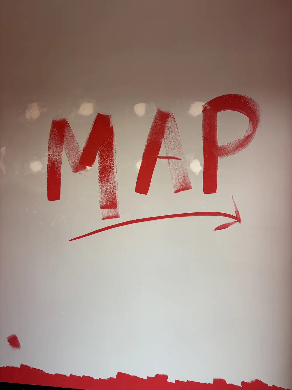 The letters MAP hand-painted in red on a white wall, with a red arrow swoosh underneath