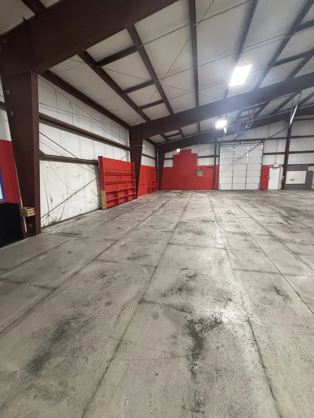 Red-painted side wall with empty shelving units and the loading door at the far end of the building